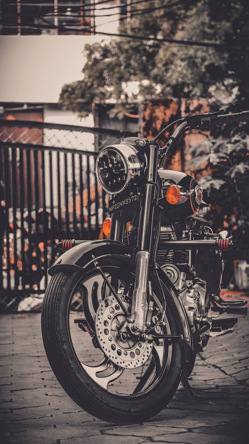 Vintage black motorcycle front view featuring a round chrome headlight and orange signals on a cobblestone path.