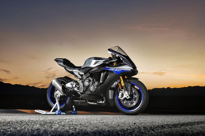 Silver and blue Yamaha R1M sportbike on a stand at sunset with desert mountains in the background scene.