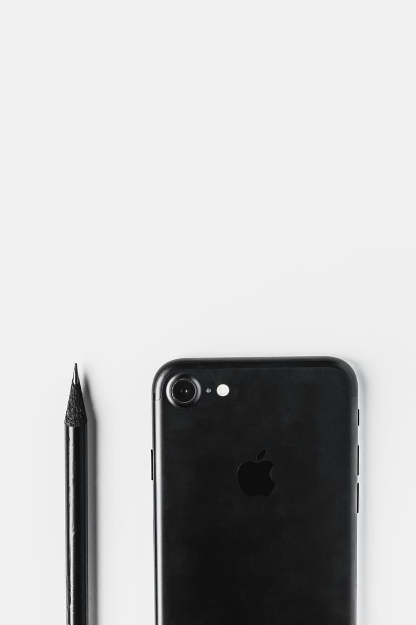 Black smartphone and graphite pencil lie on a white background in a minimalist overhead flat lay composition.