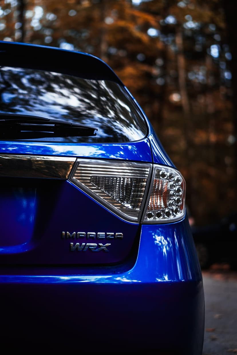 Blue Subaru WRX taillight close-up against a background of blurred orange autumn trees and forest foliage.