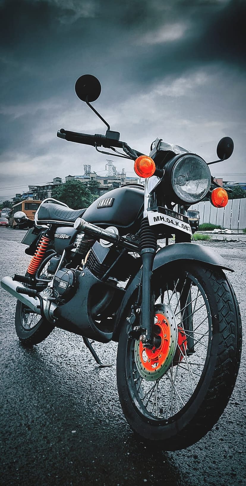 Black Yamaha RX100 motorcycle with orange signals parked on a wet asphalt street under a dark, cloudy sky.