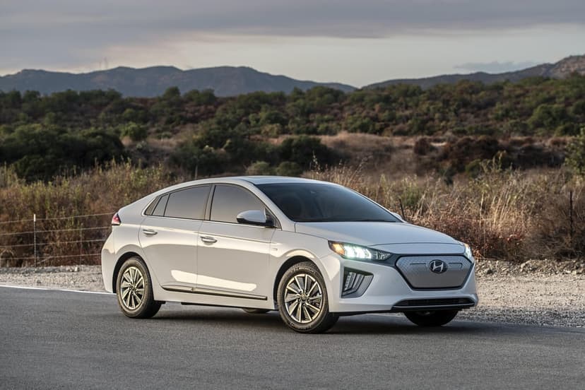 White Hyundai Ioniq Electric car on a road with hilly green landscapes and soft sunset lighting in the background.