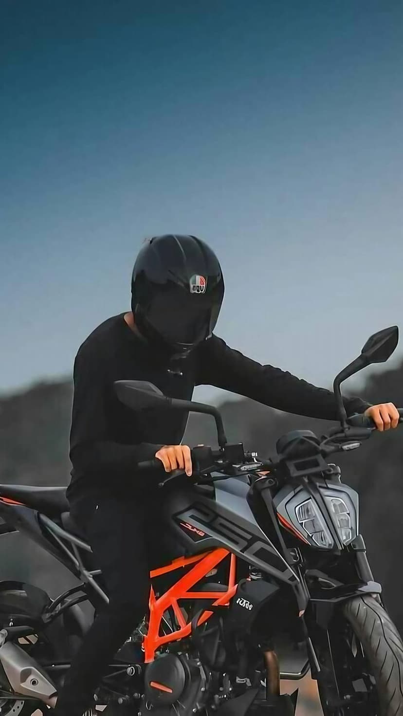 Rider in black gear sits on a black KTM Duke 250 motorcycle with orange accents under a bright blue sky.
