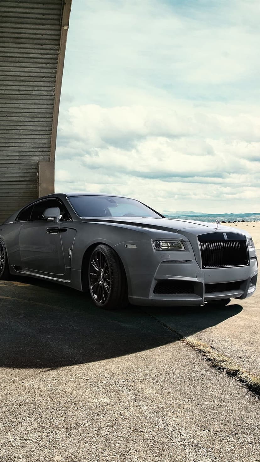 Rolls-Royce Wraith with matte grey paint and black rims parked on asphalt under a cloudy sky near the ocean.