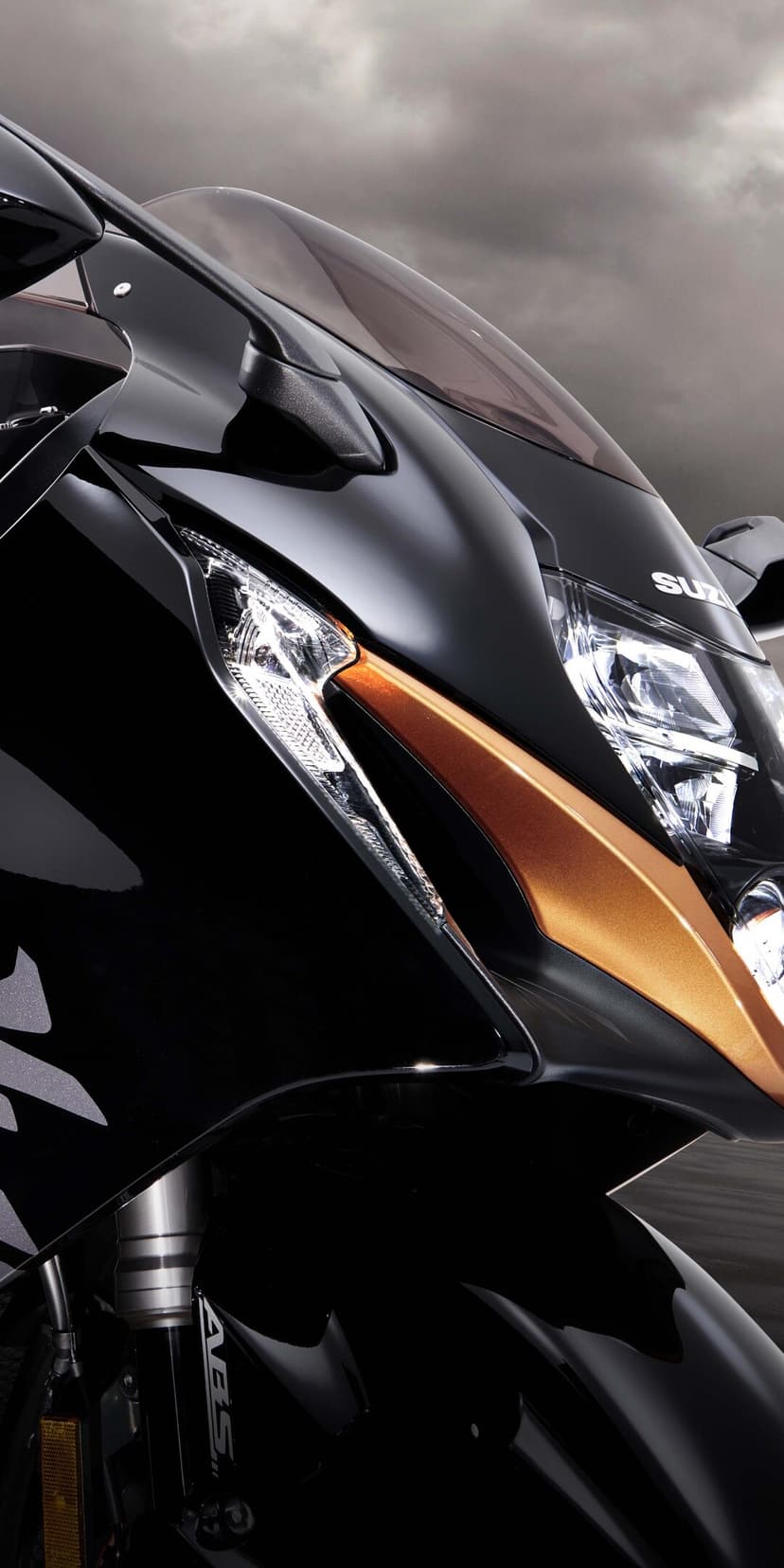 Front fairing of a black and copper Suzuki Hayabusa motorcycle with a crystalline headlight under a moody sky.