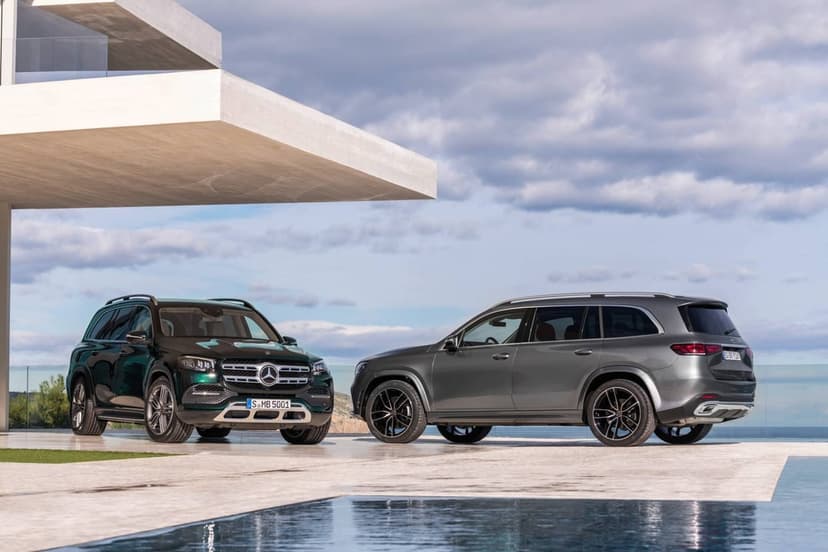 Emerald green and grey Mercedes-Benz GLS SUVs parked by a white villa and pool under a cloudy sky.