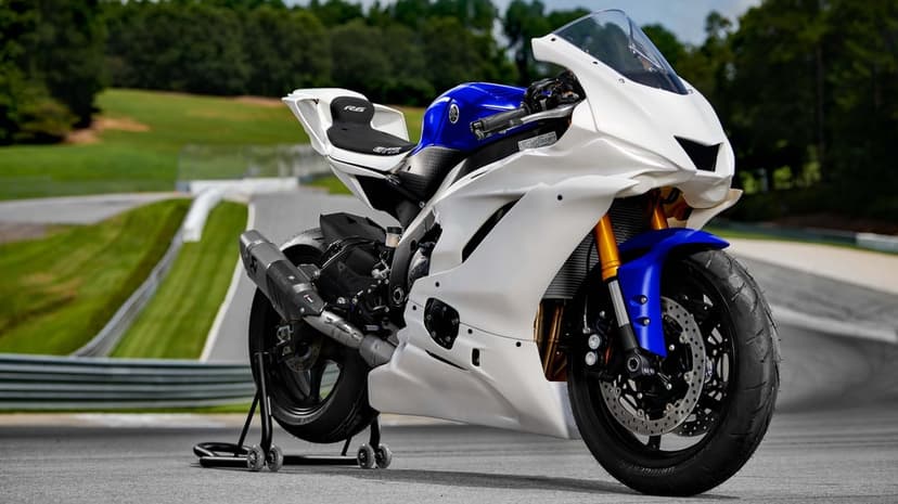 White and blue Yamaha R6 motorcycle on a rear stand at a race track with green hills in the background.