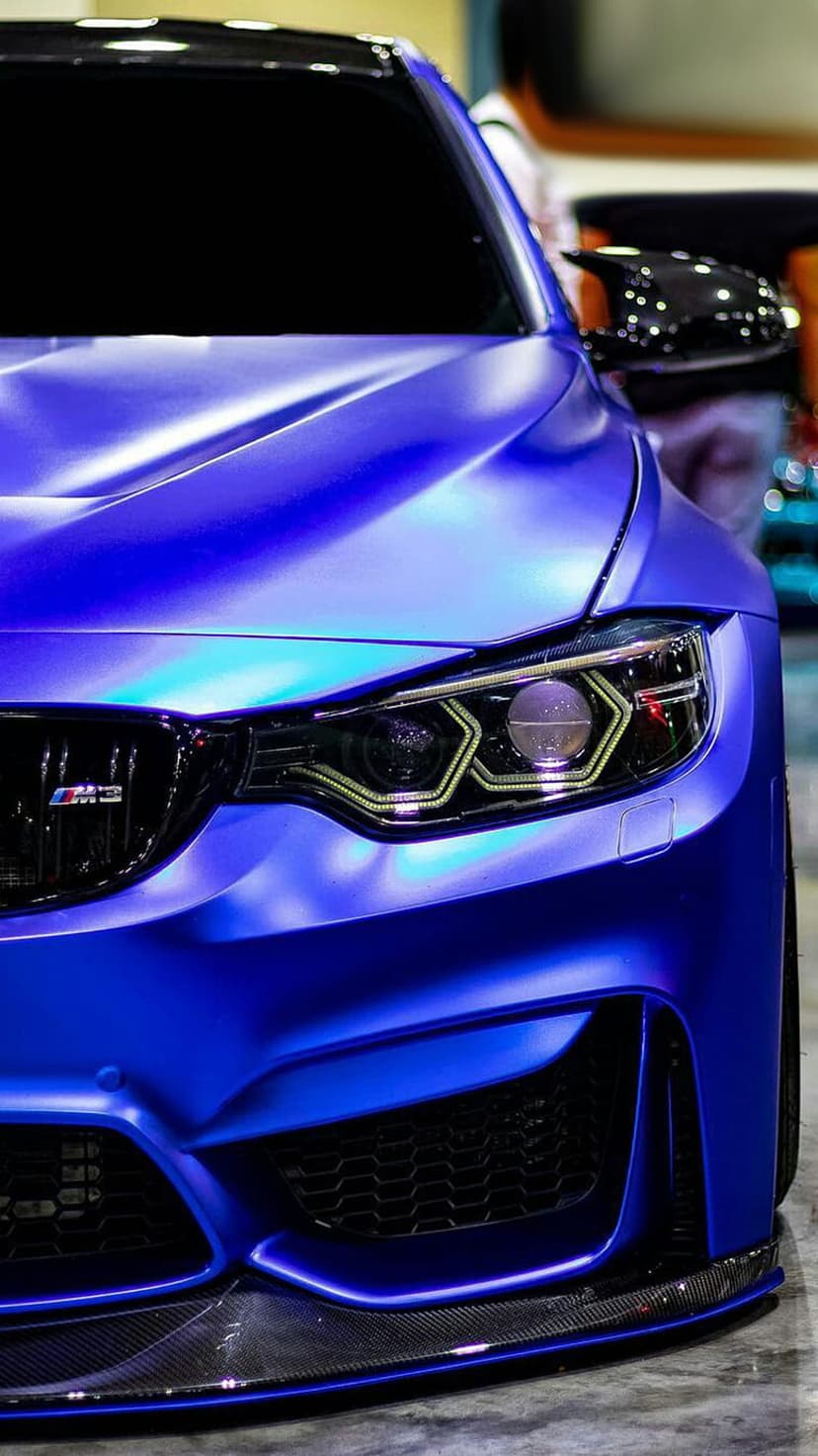 BMW M4 with matte blue paint, hexagonal LED headlights, and a carbon fiber front splitter at a low camera angle.