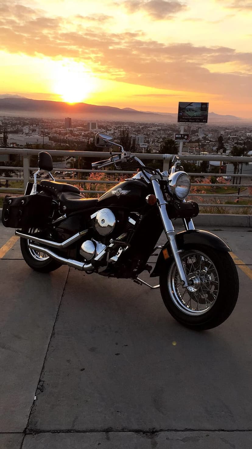 Black cruiser motorcycle with chrome accents parked on concrete overlooking a golden sunset cityscape and mountains.
