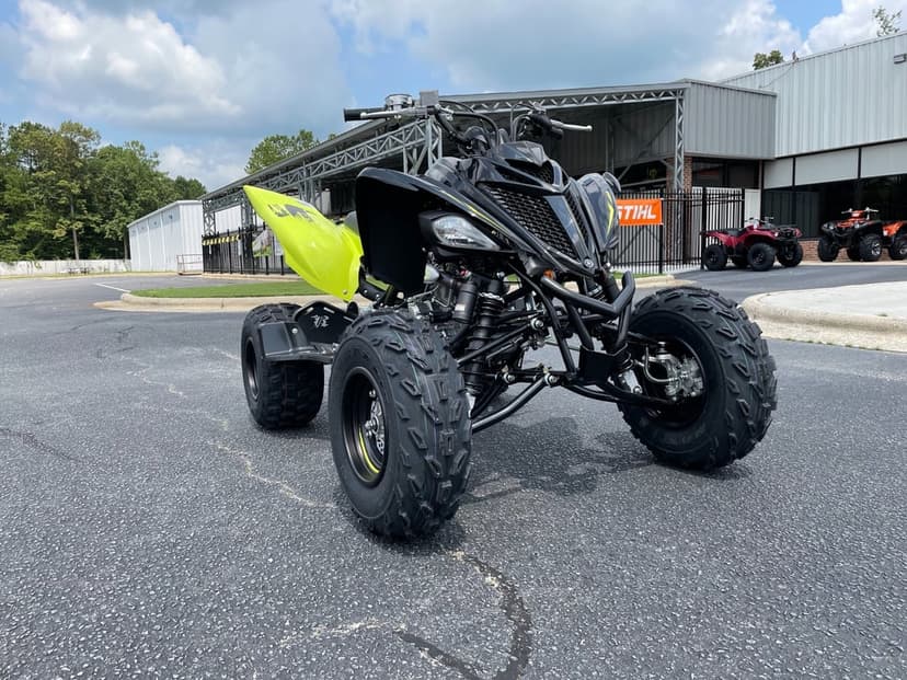 Black and lime green Yamaha Raptor sport ATV parked on an asphalt lot under a bright cloudy sky.