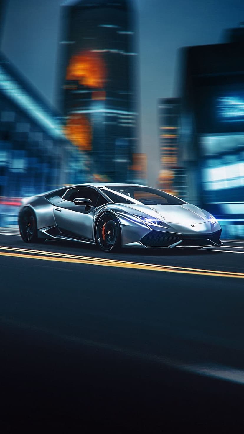 Silver Lamborghini Huracan with glowing headlights speeds past blurry city skyscrapers on a wet night street.