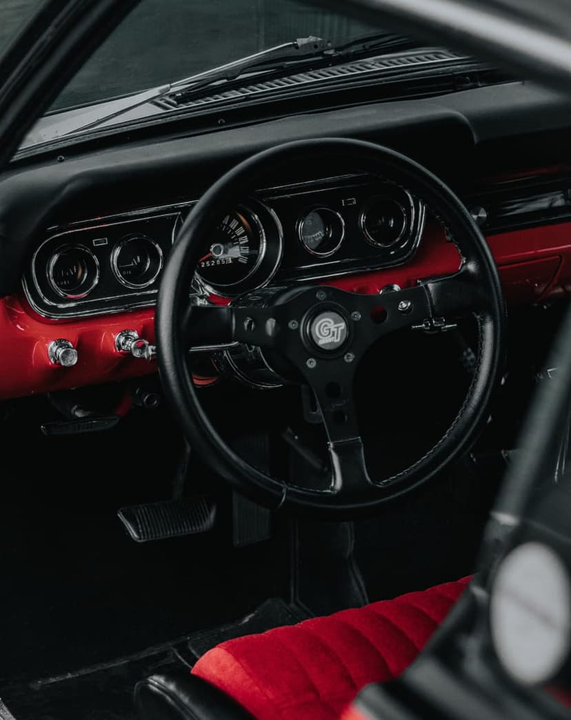 Black GT steering wheel and red dashboard with chrome analog gauges and matching leather car seat upholstery.