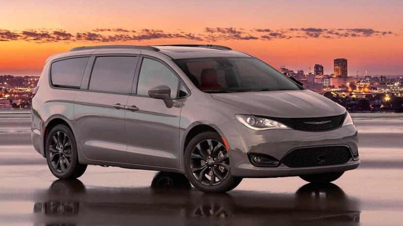 Gray Chrysler Pacifica parked on a reflective surface with a vibrant orange sunset city skyline background.