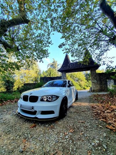 White BMW parked under leafy archway by old stone gate