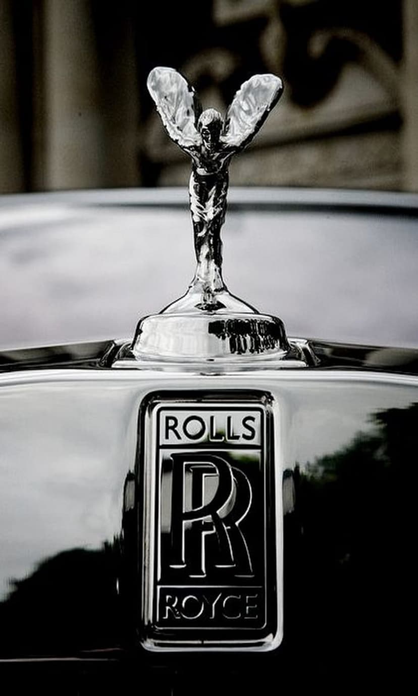 Spirit of Ecstasy mascot and Rolls-Royce badge glisten on a polished car hood in high-contrast monochrome.