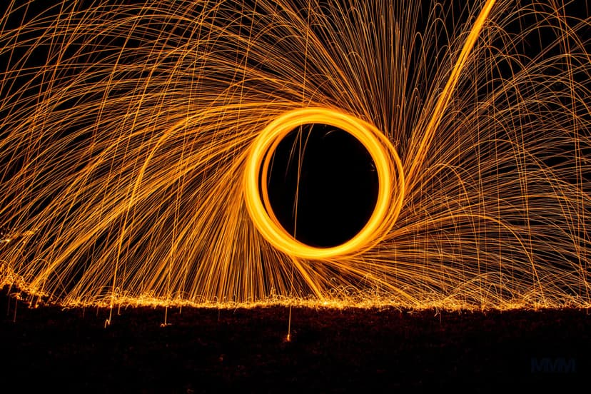 Glowing orange ring of burning steel wool emits thousands of bright sparks against a pitch black night sky.