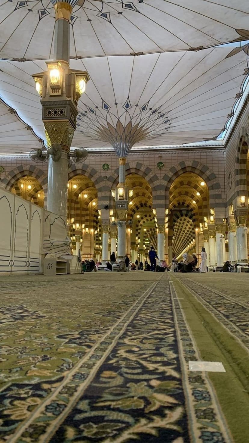 Retractable umbrellas shade ornate columns and patterned carpets inside the Prophet's Mosque in Medina, Saudi Arabia.