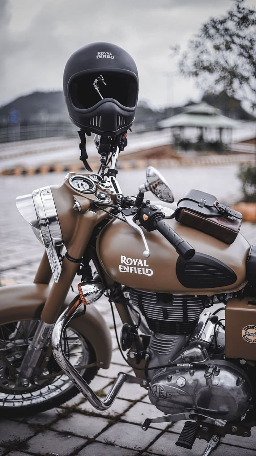 Matte brown Royal Enfield motorcycle with a leather saddlebag on the tank and a retro helmet on the handlebars.