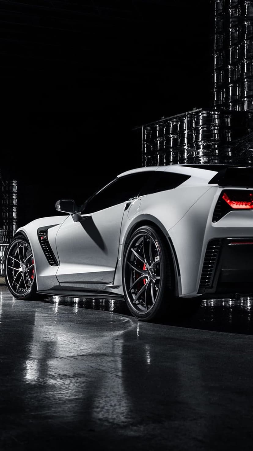 White Corvette Z06 supercar stands on a wet reflective showroom floor under dramatic industrial lighting.
