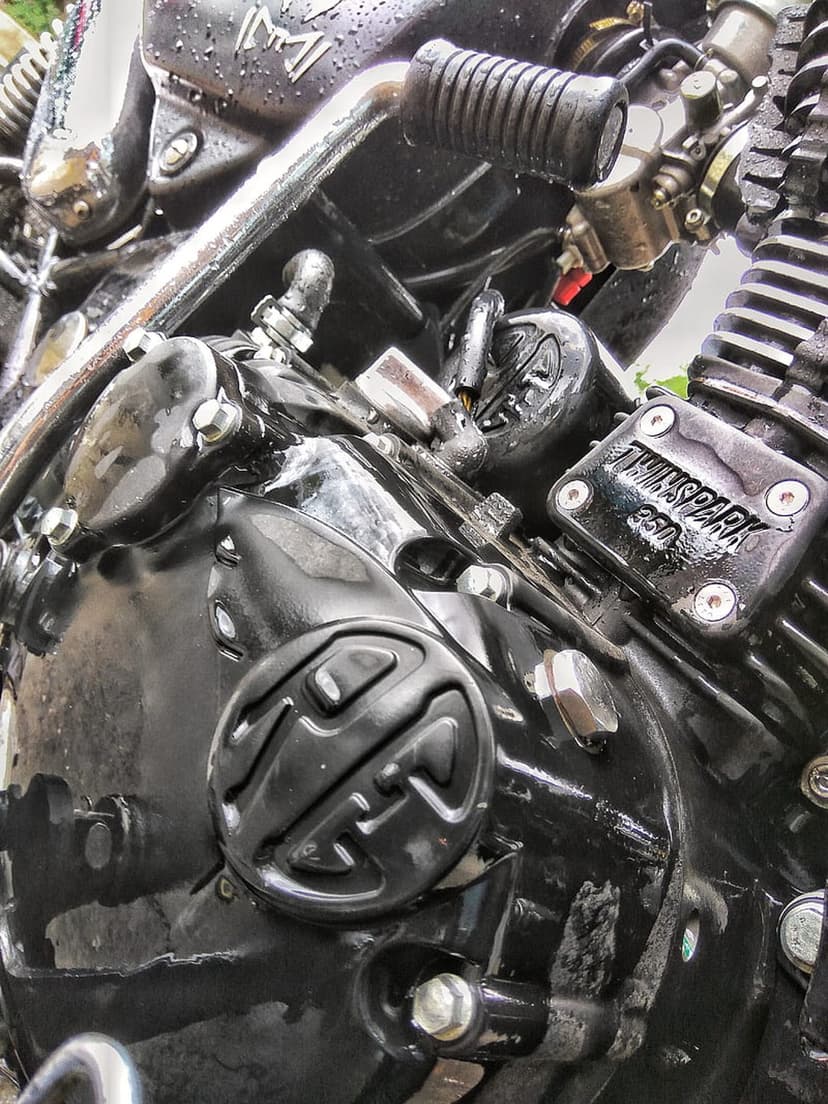 TwinSpark 350 motorcycle engine featuring glossy black metal, mechanical bolts, and scattered water droplets.