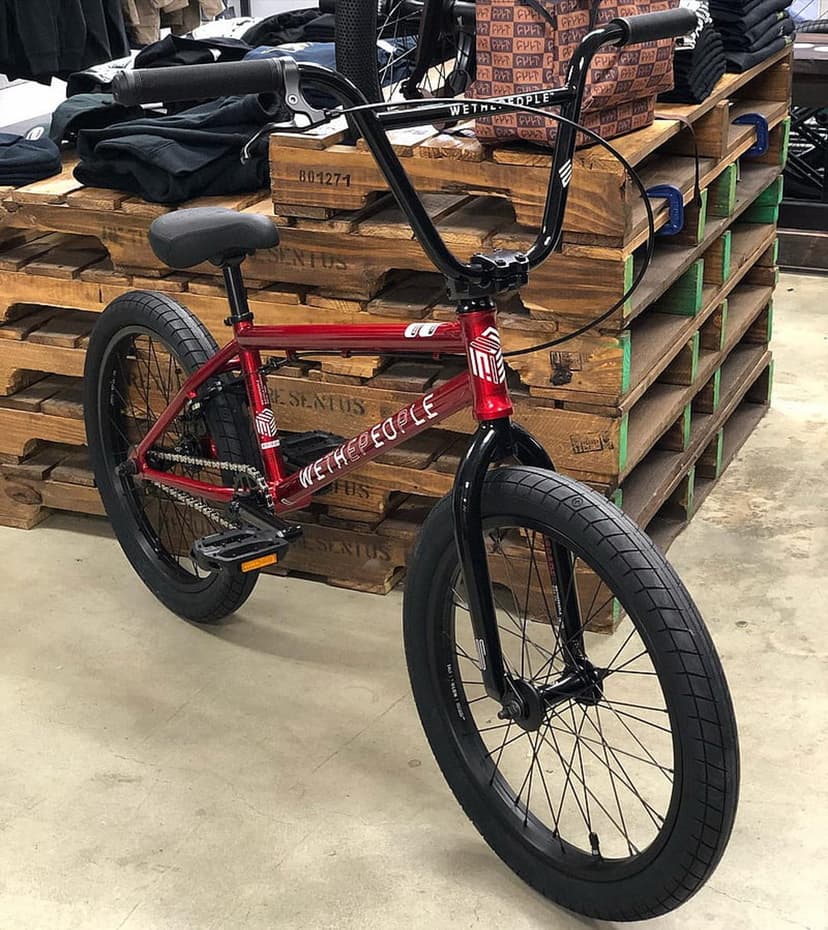 Red Wethepeople BMX bike with black tires and handlebars stands on a wooden pallet in an indoor studio setting.