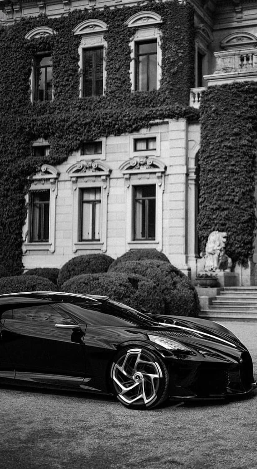Black supercar parked on a lawn in front of a historic stone mansion covered in thick climbing ivy vines.