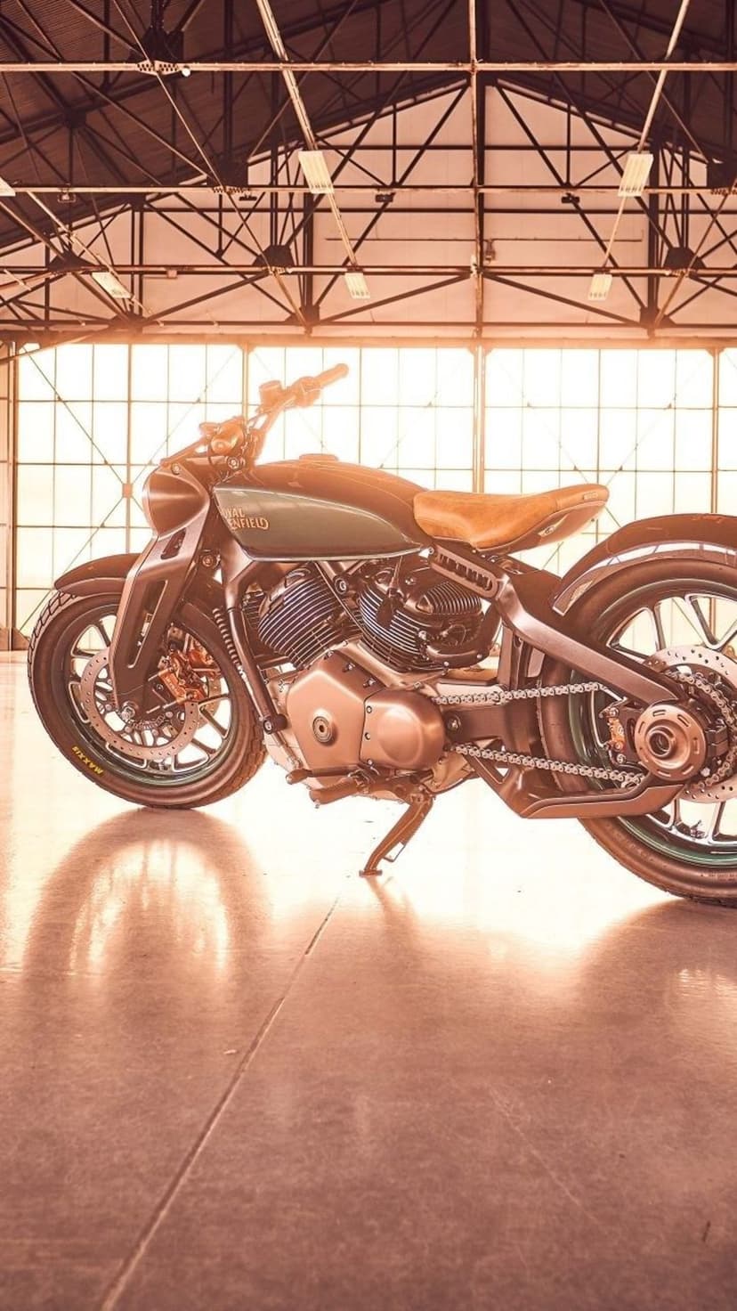 Vintage motorcycle with a green fuel tank and leather seat inside a warehouse with large windows and metal beams.