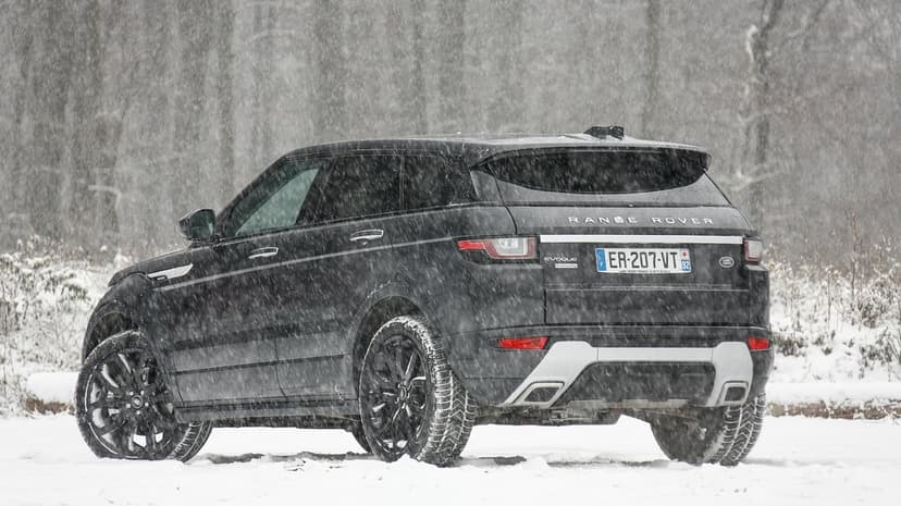 Black Range Rover Evoque SUV parked in a heavy snowstorm with falling snow and a winter forest background.
