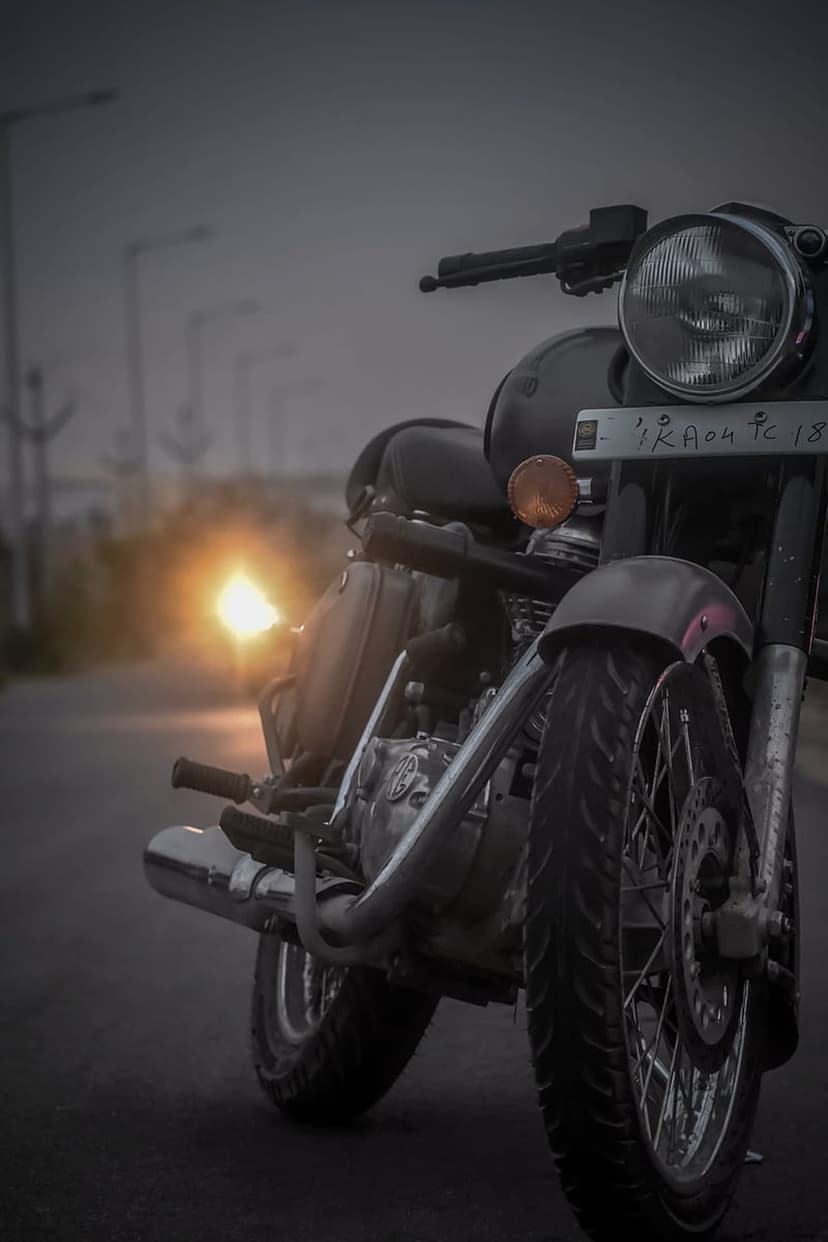 Vintage motorcycle parked on a deserted road during a hazy sunset with golden chrome reflections and sun flare.