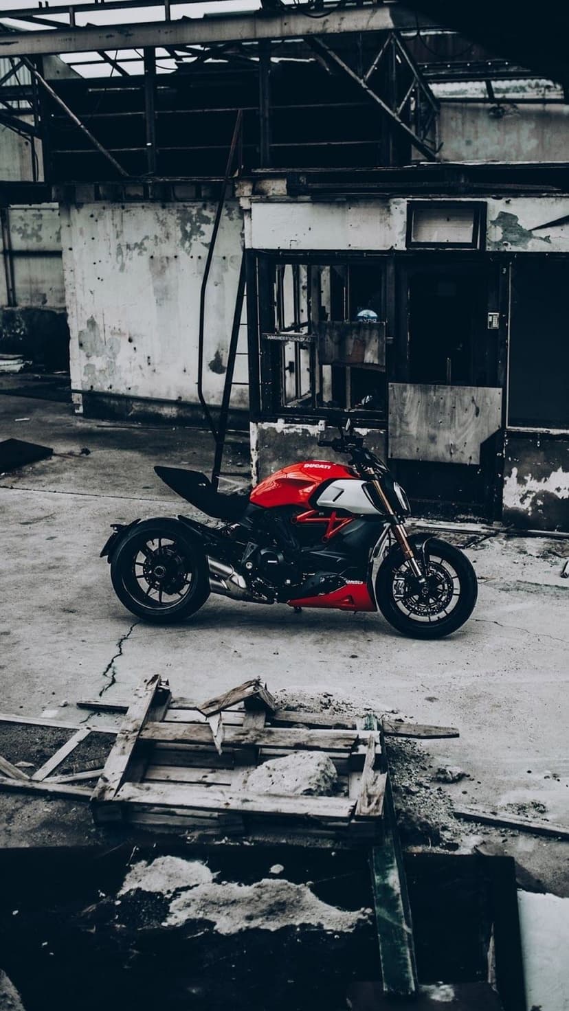 Red Ducati sportbike parked in a desolate industrial courtyard with weathered brick walls and decaying structures.