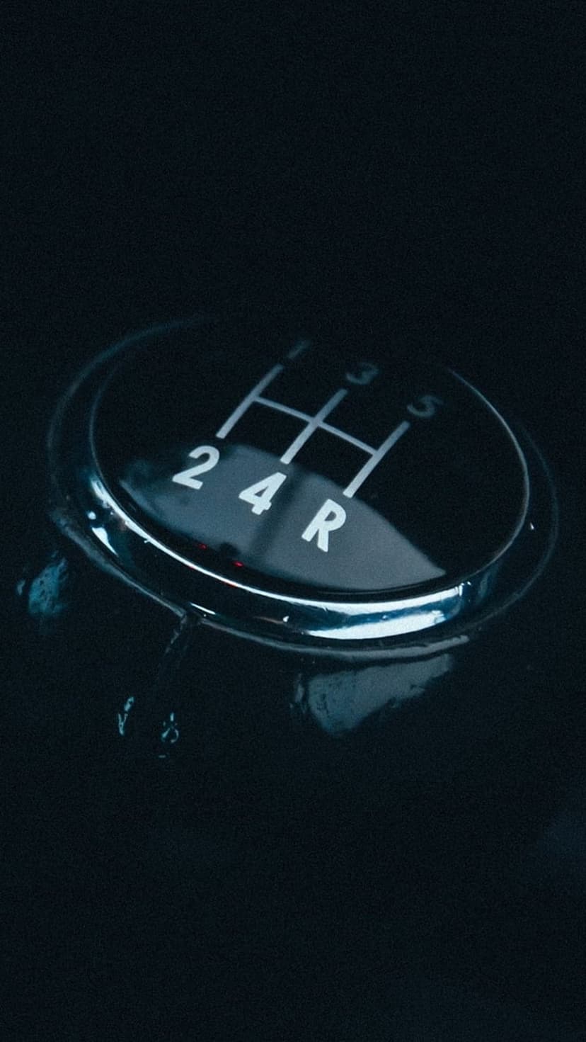 Manual five-speed gear shift knob with white illuminated numbers and a polished chrome trim in a dark car interior.