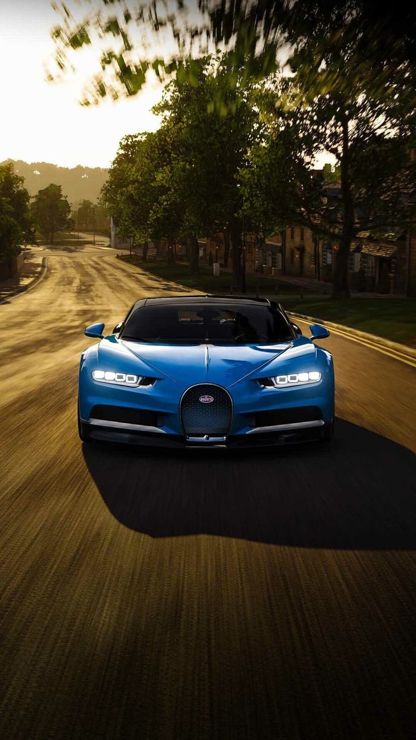 Front view of a blue Bugatti Chiron driving on a blurred road during golden hour with trees in the background.