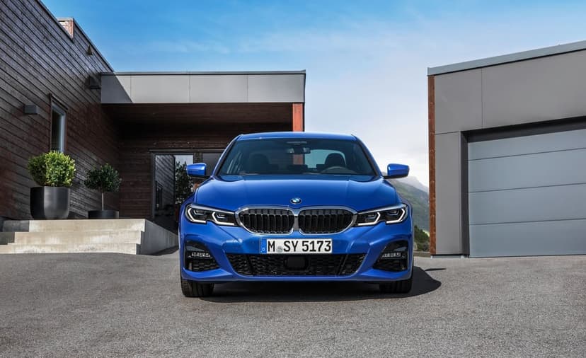 Blue BMW sedan parked on a driveway in front of a modern house with wood and grey siding under a clear sky.