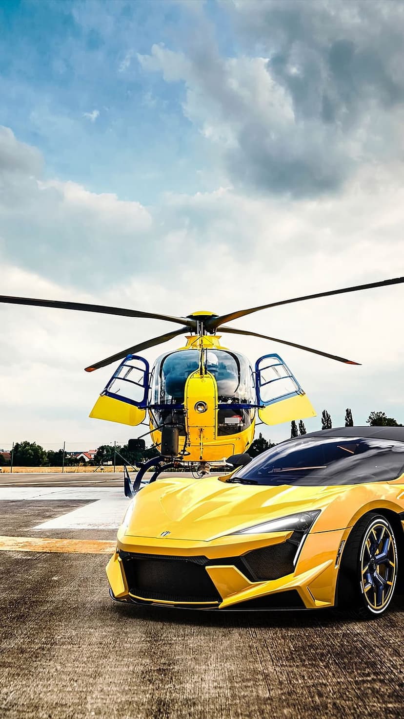 Yellow supercar and matching helicopter parked on an asphalt runway under a cloudy sky during the daytime.