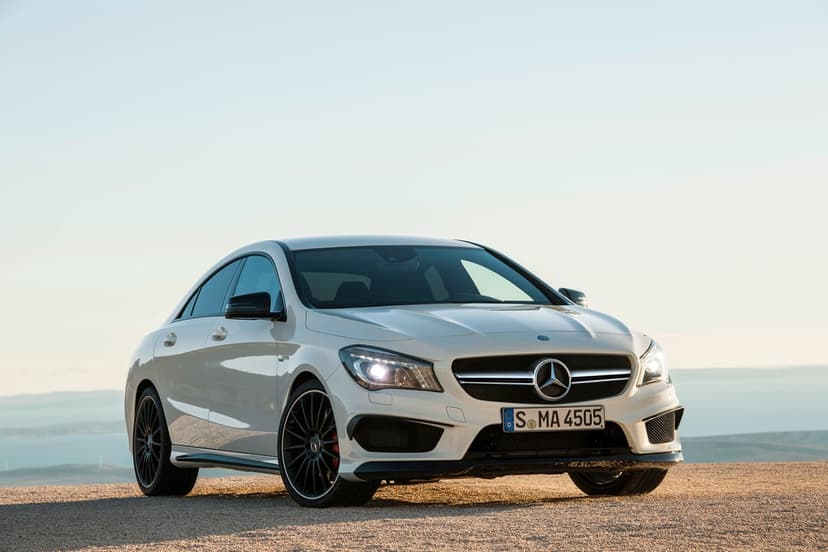 White Mercedes-Benz CLA 45 AMG parked on a gravel path against a clear light blue sky during daylight.