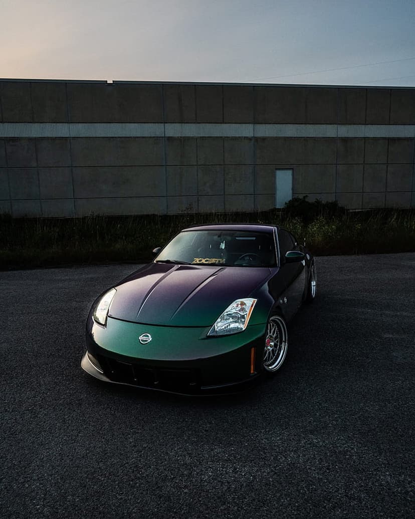 Nissan 350Z with green and purple iridescent paint parked on asphalt at dusk near an industrial backdrop.
