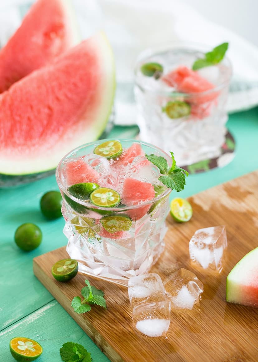 Chilled watermelon drink with lime and mint on a wooden board with melting ice cubes in a vertical composition.