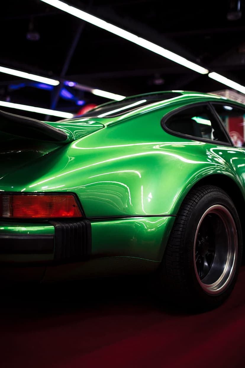 Porsche 911 rear fender in metallic green with a red taillight and black spoiler under bright studio lights.
