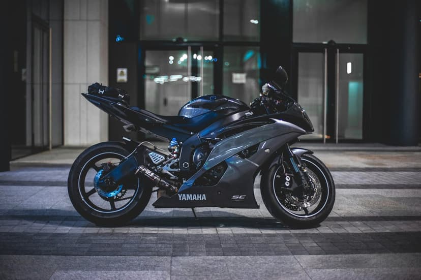 Dark gray Yamaha motorcycle parked on a paved urban walkway beside a modern glass building at night.
