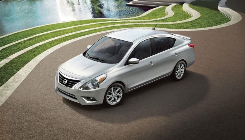 Silver sedan parked on a curved walkway beside a pool and manicured grass under soft daylight.