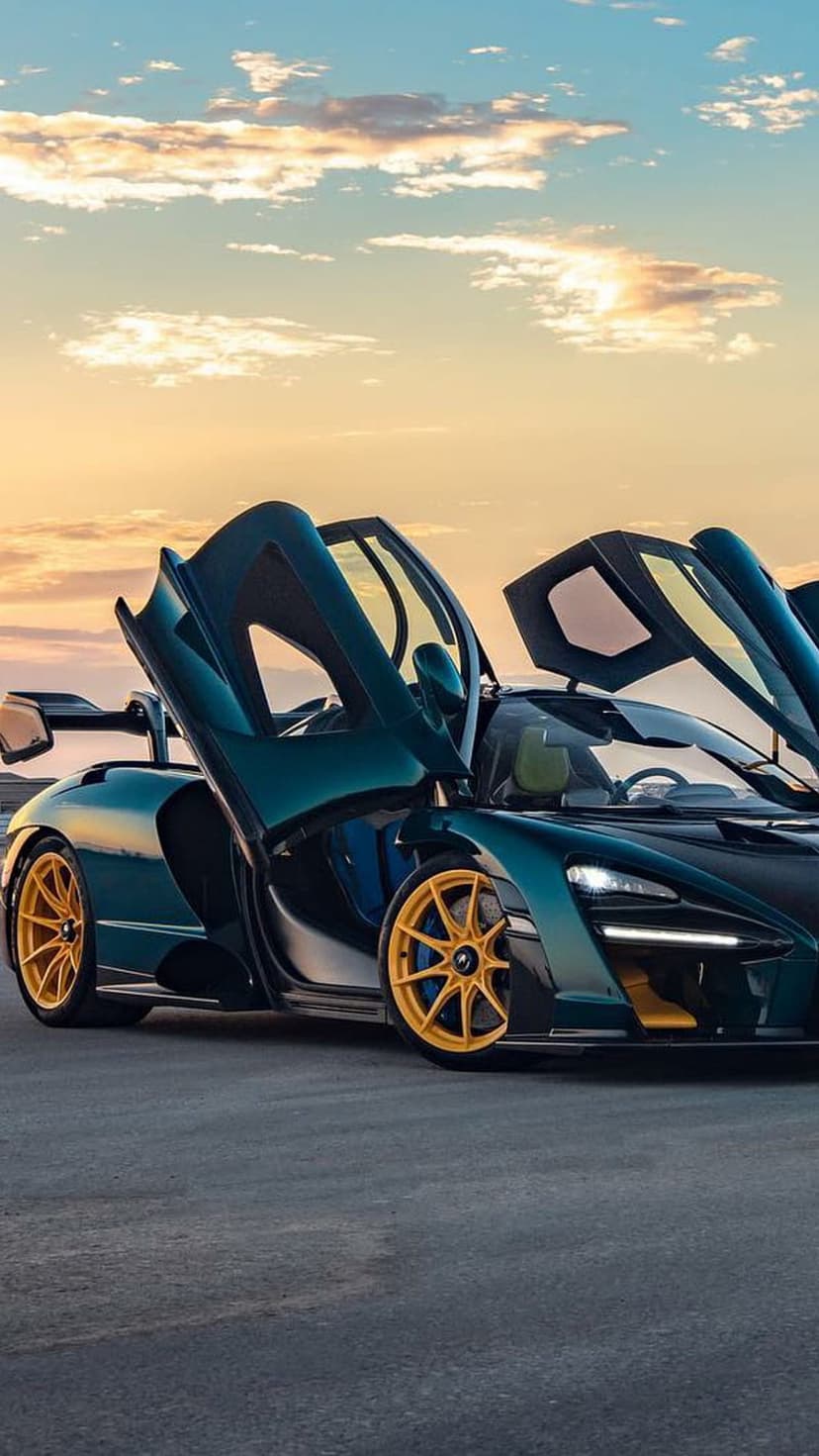McLaren Senna with teal paint and gold rims parked on asphalt as sun sets behind open dihedral doors.