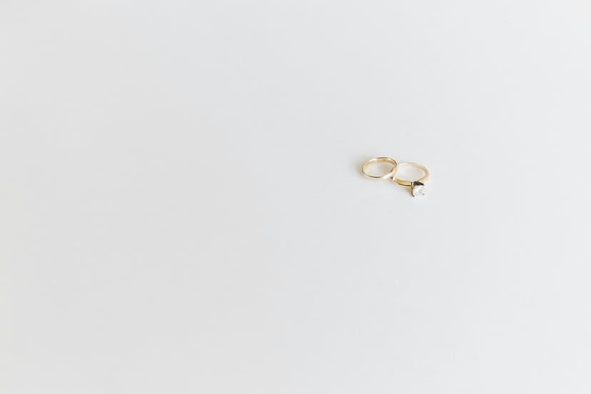 Two gold rings, including one with a small diamond, sit side-by-side on a seamless white studio background.