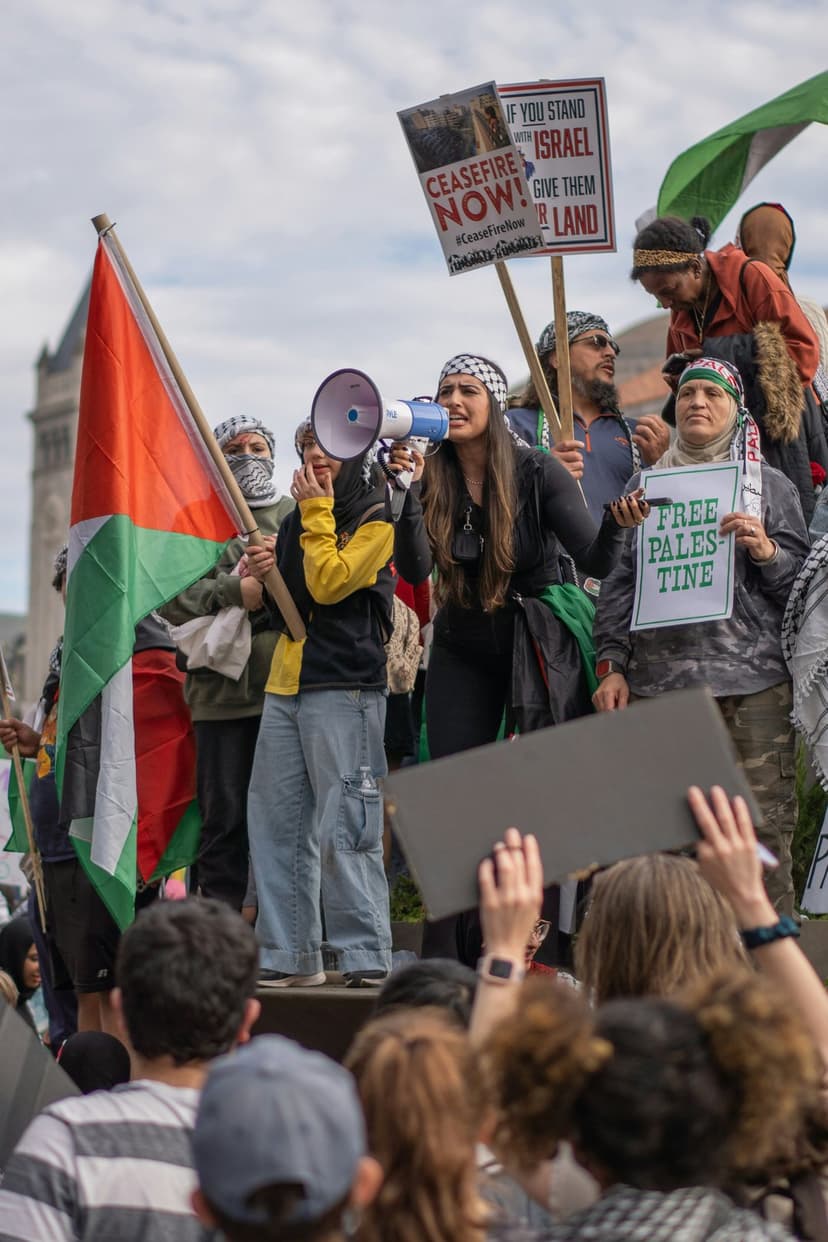 Woman leads a protest with a megaphone while supporters hold Palestinian flags and ceasefire signs in a city street.