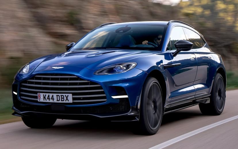 Blue Aston Martin DBX707 SUV driving on a scenic mountain road with motion blur and metallic blue finish.