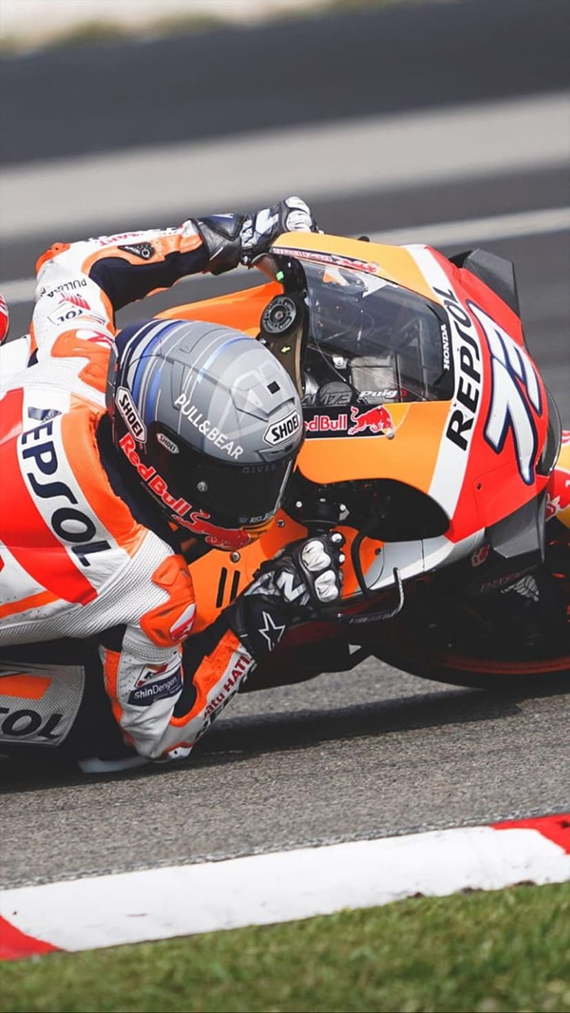 MotoGP racer in orange leathers leans a Honda Repsol motorcycle deep into a sharp turn on a blurred paved track.