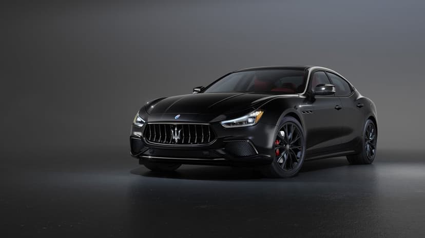 Black luxury sedan with a trident grille and red brake calipers in a dark studio setting with soft lighting.