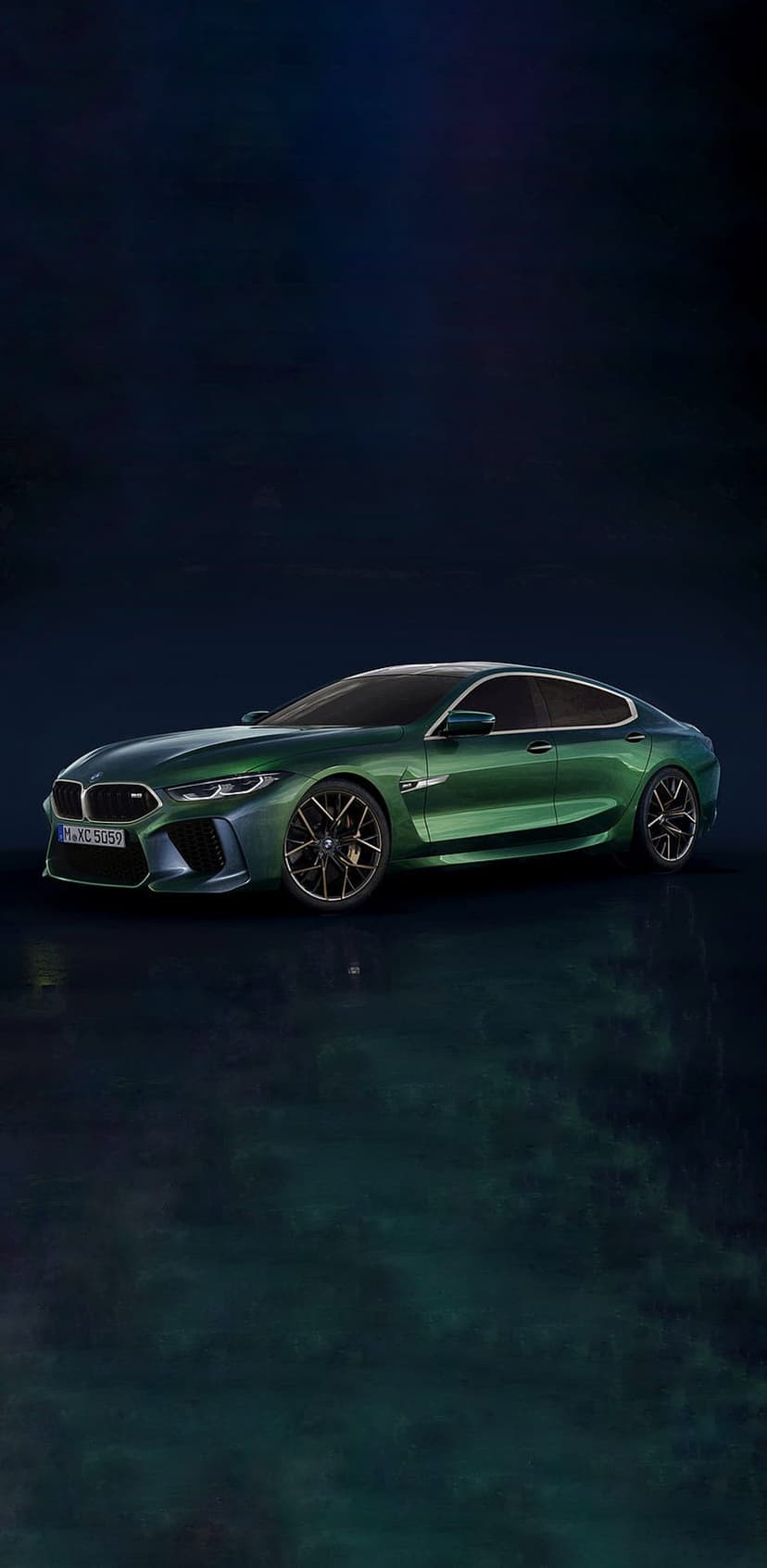 BMW M8 Gran Coupe in metallic green parked on a dark reflective floor with dramatic studio lighting and shadows.