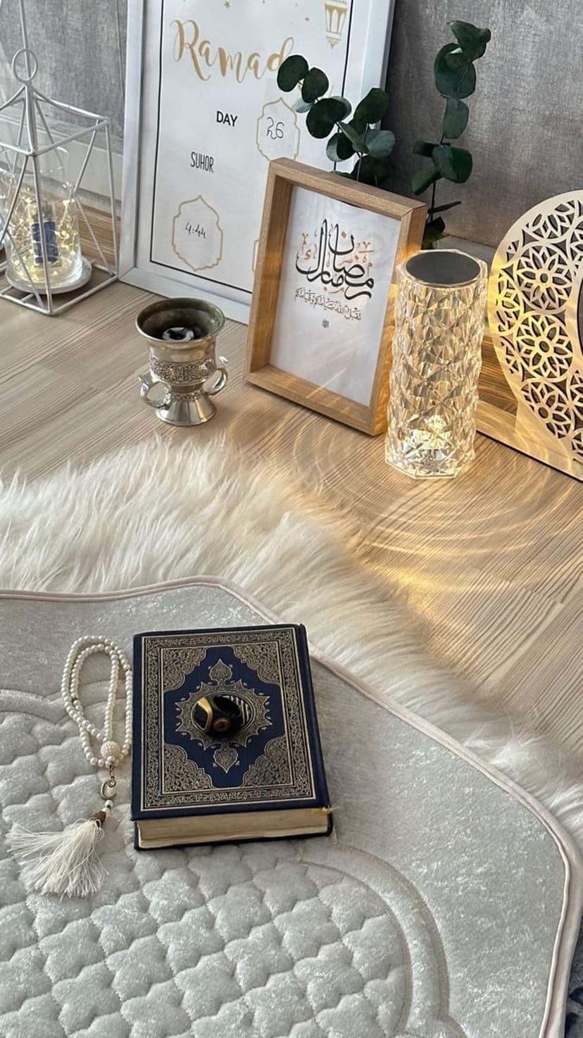 Plush prayer rug with an open Quran, white tasbih beads, and a glowing lantern in a warm spiritual setting.