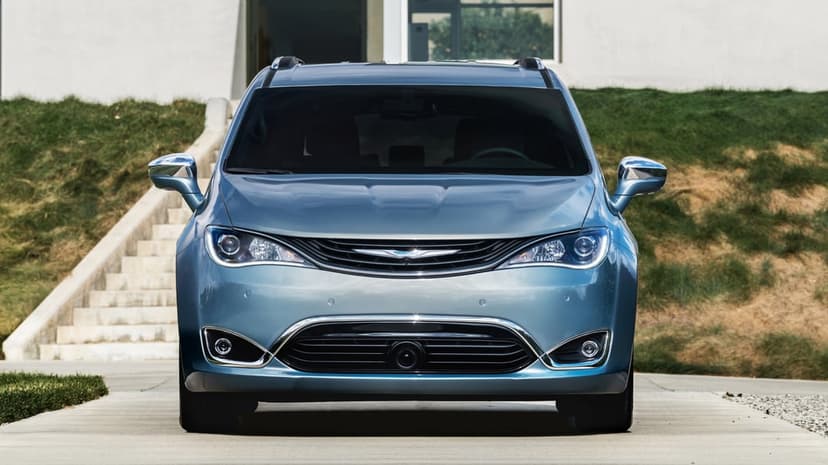 Blue Chrysler Pacifica minivan parked on a clean concrete driveway with a white modern building in the background.