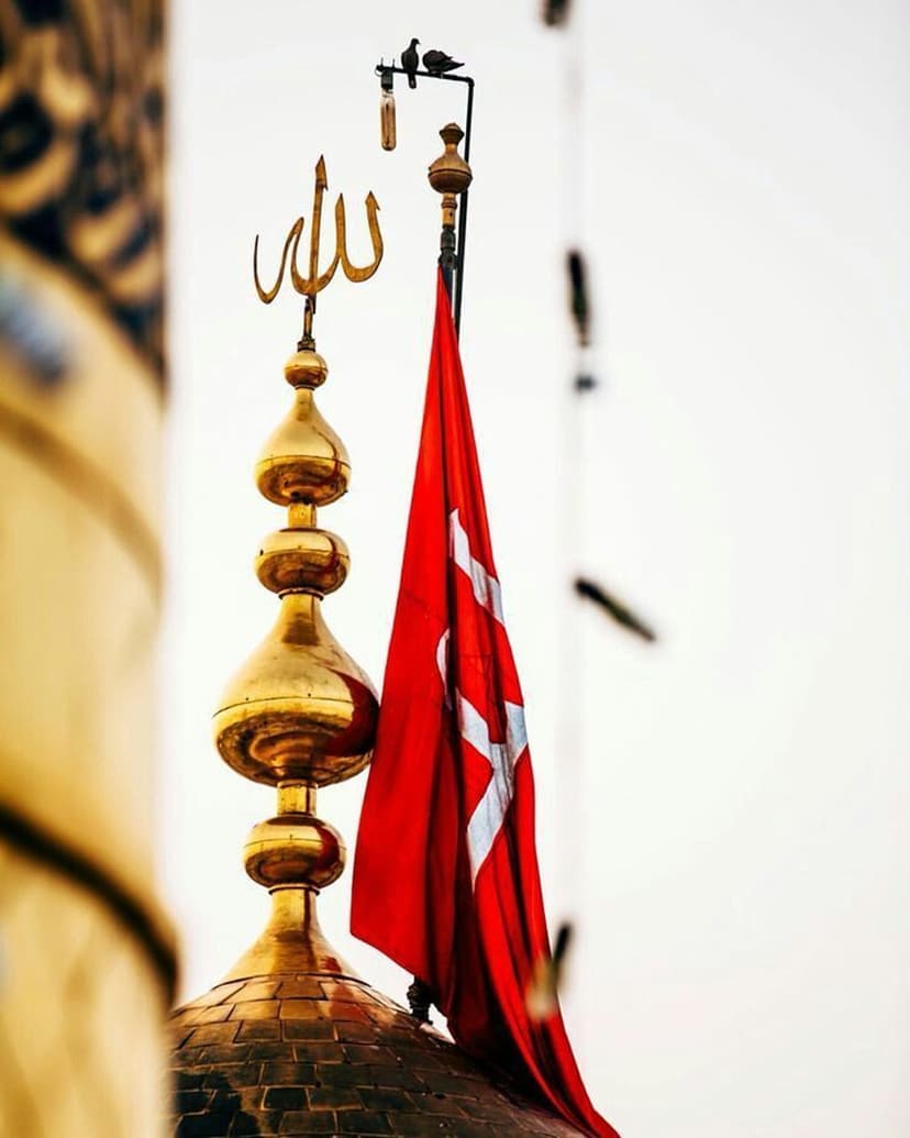 Golden mosque dome featuring Allah calligraphy beside a fluttering red flag under an overcast, grey sky.